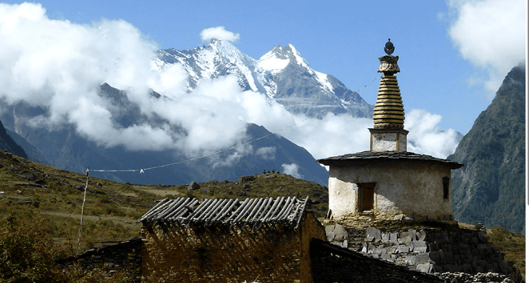 A chorten on the trail with snow peaks behind it