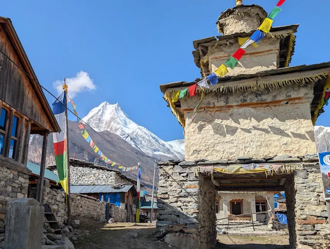 A village gateway chorten strung with prayer flags, Manaslu on the skyline beyond the stone houses